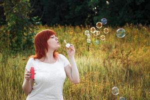 Young red haired woman blowing soap bubbles. Happy girl in nature in the sun. photo