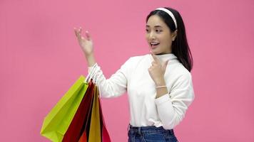 mujer joven feliz sonriendo y sosteniendo bolsas de compras y tarjeta de crédito mientras hace algunas compras en un estudio rosa foto