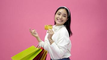 Happy Young woman smiling and hold shopping bags and credit card while doing some shopping on a pink studio background photo