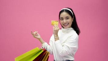 Happy Young woman smiling and hold shopping bags and credit card while doing some shopping on a pink studio background photo