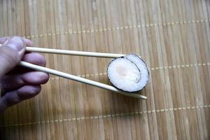 Taken with chopsticks sushi with tuna for eating. Delicious fish roll. Rice sushi roll on a mat. photo