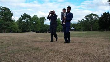 2 jovens machos asiáticos estão posando com um bebê no parque público local de luton inglaterra, reino unido video