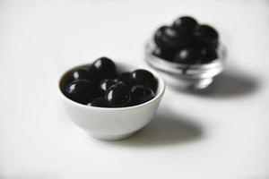 Black olives in a white and glass saucepan on a white background. photo