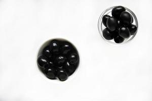 Black olives in a white and glass saucepan on a white background. photo