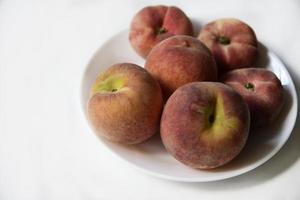 Juicy red and yellow peaches on a white plate. Delicious peaches for lunch. photo