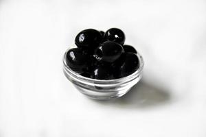 Black olives in a white and glass saucepan on a white background. photo