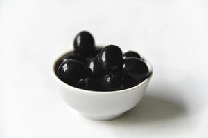 Black olives in a white and glass saucepan on a white background. photo