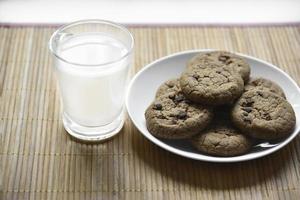 A glass glass with milk on a wooden mat with oatmeal cookies. Afternoon lunch with cookies. Sweet cookies with milk. photo