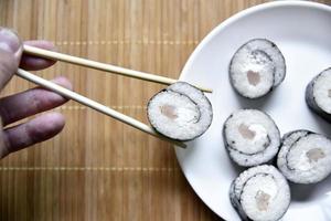 Taken with chopsticks sushi with tuna for eating. Delicious fish roll. Rice sushi roll on a mat. photo