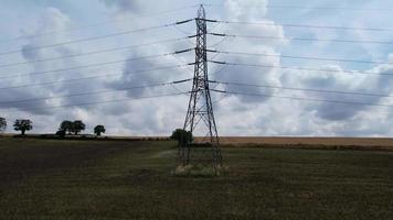 postes de suministro de energía de alto voltaje con cables que recorren las tierras de cultivo y el campo británicos, vista aérea de ángulo alto por la cámara de drones video