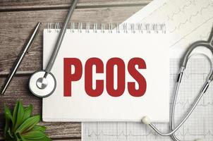 Text PCOS on notebook with stethoscope and pen on wooden background photo