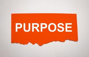 On a bright grey background, a sheet of torn paper with the text PURPOSE. photo