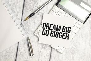 Text Think Big Do Bigger on paper card and calculator on wooden background photo