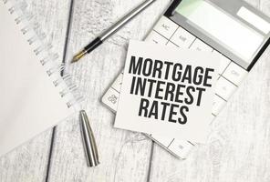 tasas de interés hipotecario de texto en tarjeta de papel y calculadora sobre fondo de madera foto