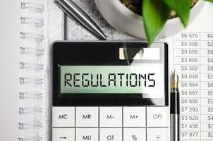 regulations word on calculator display and pen, charts on wooden background photo