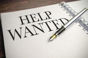 Text HELP WANTED on paper notepad and pen on wooden background photo