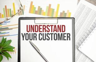 Paper with UNDERSTAND YOUR CUSTOMER on a table with charts, glasses and pen photo