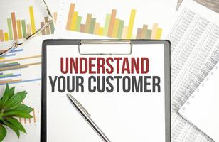 Paper with UNDERSTAND YOUR CUSTOMER on a table with charts, glasses and pen photo