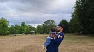 il padre pakistano asiatico tiene in braccio il suo bambino di 11 mesi nel parco locale video