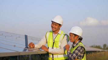 Asian Young technician engineer man and Female supervisor in white helmet, They are discussing quality of mounting of panels in solar farm