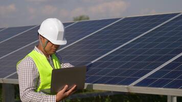 un ingénieur inspecteur asiatique utilise un ordinateur portable tout en vérifiant l'efficacité du soleil pour examen sur la construction de panneaux solaires video