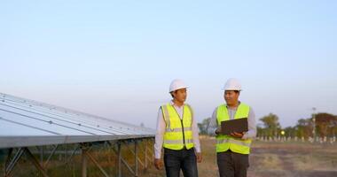 un ingénieur inspecteur asiatique et un jeune technicien utilisent un ordinateur portable, deux ingénieurs discutent et vérifient l'efficacité de la construction de panneaux solaires pour examen avec un ordinateur portable video