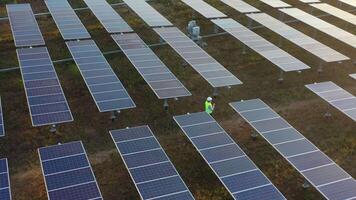 Rotate Shot, Aerial drone view, Flight over solar panel farm, young engineer wearing helmet checking on operation of sun and cleanliness of photovoltaic solar panels at sunset video