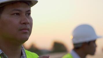 Nahaufnahme, Gesicht eines jungen Ingenieurs mit weißem Helm, während er bei Sonnenuntergang den Betrieb der Sonne und die Sauberkeit der Photovoltaik-Solarmodule überprüft video