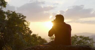 rallentatore in controluce, giovane viaggiatore con zaino e sacco a pelo seduto su scogliere rocciose usa la fotocamera digitale per scattare una foto mentre sei nella foresta video