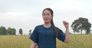 retrato de mulher jovem agricultor asiático feliz olhando para a câmera e acenando com as mãos no arrozal. video