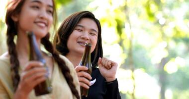 Close up shot, Young beautiful Asian woman and girl friend relaxing while camping in forest, standing to dancing and drinking beer with happy together video