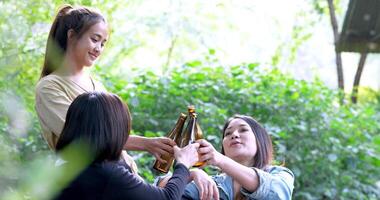 Handaufnahme, Gruppe schöner asiatischer Freundinnen, Reisende, die sich in Campingstühlen im Bach entspannen, sie jubeln und trinken Bier während des Campings, reden mit Spaß und glücklich zusammen video