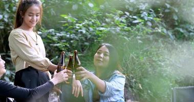 Handaufnahme, Gruppe schöner asiatischer Freundinnen, Reisende, die sich in Campingstühlen im Bach entspannen, sie jubeln und trinken Bier während des Campings, reden mit Spaß und glücklich zusammen video