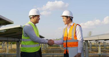 asiatischer junger technikermann und ingenieur, der hände schüttelt und glücklich lächelt, während er im solarpark arbeitet, hintergrund des sonnenkollektors video