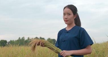 ritratto di felice asiatico giovane contadino donna che tiene riso e guardando la fotocamera nella risaia. video