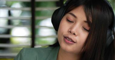 Close up shot, Pretty young Asian woman sitting and enjoy to listening musice from wireless headphone and singing together with smartphone at cafe. People, relaxing and lifestyle concept. video