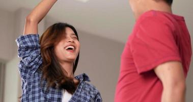 asiatisches junges lustiges ehepaar, das spaß hat und im wohnzimmer tanzt. Schöne glückliche Frau und gutaussehender Mann tanzen und lachen im neuen Zuhause, glückliches Familienkonzept video