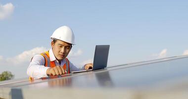 Young Asian technician man checking operation of sun and cleanliness of photovoltaic solar panel and typing on laptop computer while working in solar farm video