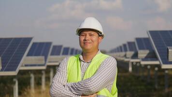 Portrait Asian young engineer wear white helmet standing and crossing arms with smile at solar farm, solar panel in background video