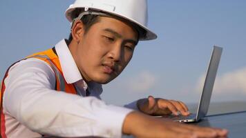 Close up, Young Asian technician man checking operation of sun and cleanliness of photovoltaic solar panel and typing on laptop computer while working in solar farm video