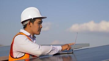 Junger asiatischer Techniker, der den Betrieb der Sonne und die Sauberkeit des Photovoltaik-Solarmoduls überprüft und auf einem Laptop-Computer tippt, während er im Solarpark arbeitet video