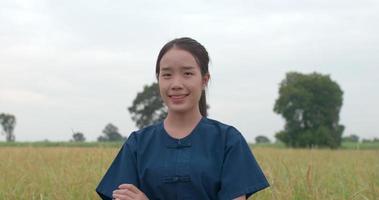 tiro em câmera lenta de mulher jovem agricultor asiática feliz olhando para a câmera e os braços cruzados no arrozal. video