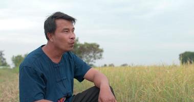 Porträtaufnahme eines glücklichen asiatischen Bauern in einem blauen Kleid, der auf dem Reisfeld pfeift. video