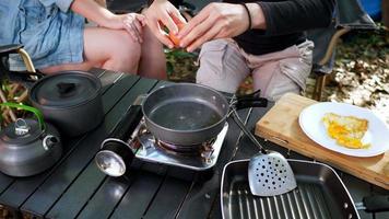 gros plan, une main féminine met un œuf sur la casserole en camping avec un ami, cuisine un repas facile dans le parc naturel video