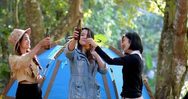 groep mooie aziatische vrouwen vrienden reizigers ontspannen aan de voorkant van de campingtent, ze staan te dansen en bier te drinken en praten met plezier en gelukkig samen video