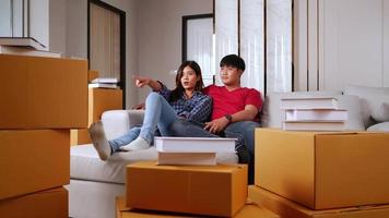 Slow motion shot, Young couple sitting on sofa bed and checking boxs after relocation in their new home, new house concept video