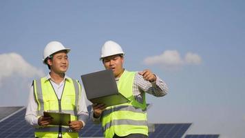 dos técnicos e ingenieros asiáticos usan una computadora portátil mientras verifican la eficiencia del sol para examinar la construcción de paneles solares y hablar juntos