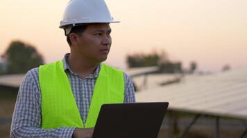 un jeune ingénieur technicien asiatique utilise un ordinateur portable tout en vérifiant l'efficacité du soleil pour examen sur la construction de panneaux solaires video