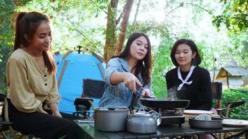 gros plan de poche, un groupe de jeunes femmes apprécient de cuisiner des repas dans une casserole avec une cuisinière à gaz à l'avant de la tente de camping dans le parc video