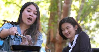mise au point sélective la main d'une jeune femme asiatique cuisinant et son amie aime préparer le repas dans la casserole, ils parlent et rient avec plaisir ensemble en camping dans le parc naturel